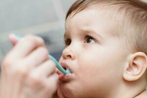 Mom helps his young son to brush his teeth photo