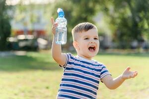 joyful child drinks clear water from a bottle on a sunny day in nature photo