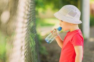 hermoso chico bebidas claro agua desde un botella en un soleado día fuera de foto