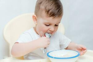 adorable baby boy eats porridge with a small spoon himself photo