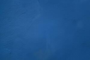 A close up photo of an exterior textured wall painted blue, surface with stucco daub, great for background