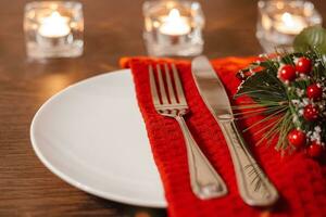 Christmas table setting. Plate and cutlery on napkin. Preparing for festive dinner. Candles burning on table on Christmas Eve. photo