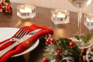 Christmas table setting. Plate and cutlery on napkin. Preparing for festive dinner. Candles burning on table on Christmas Eve. photo