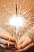 New Year celebration. Young woman holds sparkler in her hands. Christmas night. Bright sparks of fire photo