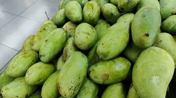 pile of big mango fruits on the shelf in local grocery supermarket, medium close up photo. photo