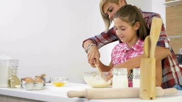 Dolly slider 4K footage of beautiful mother and young doughter cooking together at the kitchen. They are preparing dough for bake video