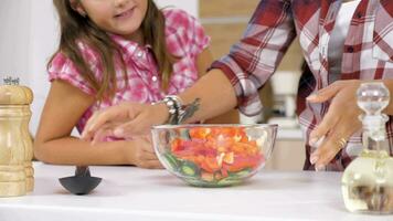 Close up of woman mixing a salad in glass bowl in the kitchen while her daughter sits next to her video