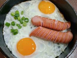 Scrambled eggs in a frying pan with fried meat sausages photo