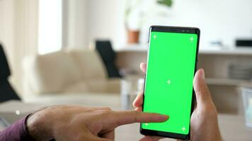 vicino su di uomo utilizzando un' moderno smartphone con verde schermo croma finto su su esso nel il suo Casa a il scrivania. dolly cursore 4k metraggio video