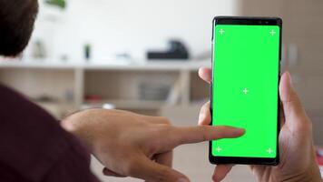 Close up of man hand touching and using a smartphone with green screen chroma mock up on it in the living room of his house video