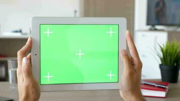 uomo Tenere un' grande digitale talbet pc con verde schermo croma modello nel orizzontale modalità a il scrivania di il suo vivente camera video