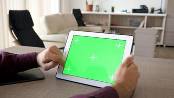 Man working on digital tablet PC with green screen mock up. The gadget is on the desk. In blurred background a comfortable living room. Dolly slider 4K footage with parallax effect video