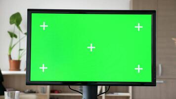 Modern Personal computer with big screen chroma mock up on the desk in living room. A man is entering the room in the background and sits on the couch while looking at his phone video