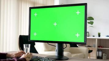 Unrecognisable man typing on personal computer keyboard with big green screen chroma mockup in the living room of his house. Dolly slider 4K footage with parallax effect video