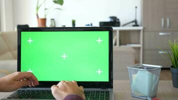 Revealing shot of man working on the computer with a chroma green screen mock up in his house. Dolly slide parallax 4K footage video