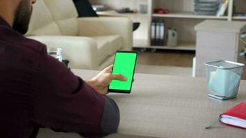 Man holding a smartphone with green screen chroma mock up in hands in his house at the desk. Dolly slider parallax 4K footage video