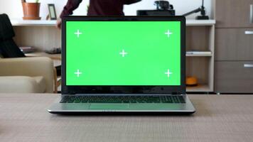 zoom i på en anteckningsbok med isolerat grön skärm och markörer för spårning i ett lägenhet. en person är gående i de bakgrund och sitter på de soffa ser i hans smartphone video