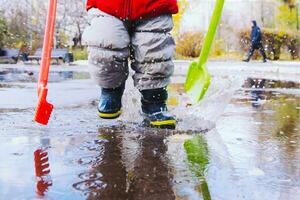 A small kid with a rake and a shovel walks in the park photo