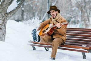 cheerful guy playing guitar in park in winter photo