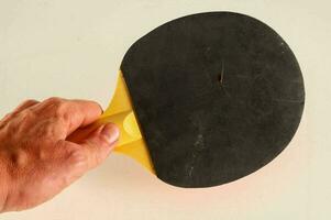 a hand holding a tenis table paddle with a black and yellow top photo