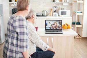 Senior couple talking with niece and daughter on online video call from kitchen. Elderly person using modern communication online internet web techonolgy. photo