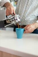 Close up of senior man hands spilling aromatic hot drink in cup during breakfast sitting in modern kitchen. Grandfather in the morning enjoying fresh brown espresso from mug, filter relax refreshment photo