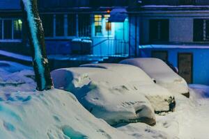 cars stand in the yard in the evening covered with snow photo