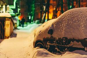 cars stand in the yard in the evening covered with snow photo