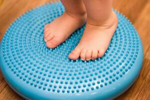 little kid massages his feet while standing on the rug photo