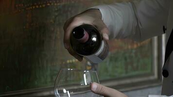 Man sommelier pouring red wine into glass, close-up photo