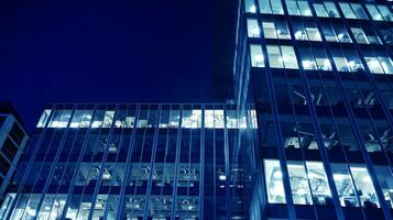 Pattern of office buildings windows illuminated at night. Glass architecture ,corporate building at night - business concept. Blue graphic filter. photo