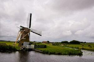 a windmill is next to a river in a field photo