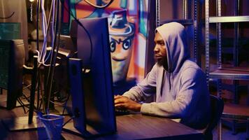 Zoom in shot on african american hooded hacker targeting vulnerable unpatched connections, seeking to compromise digital devices and steal valuable sensitive data from them video