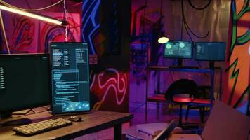 ordinateur écrans montrant malware développement code dans fatigué souterrain cachette avec graffiti peint sur des murs. PC système équipement utilisé pour cybercriminel activité dans néon allumé endroit video