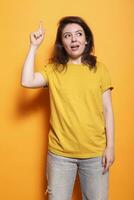 Positive woman standing over isolated orange background with index finger pointing up. In studio, Caucasian female adult having a great idea while gesturing and looking upwards. photo