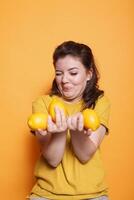 In the studio, female individual with a goofy face holding yellow citrus fruits. Young woman displaying a bunch of fresh raw natural lemons for a vitamin rich snack. photo