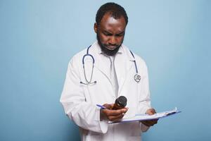 Doctor with stethoscope inspects prescription pill bottle while holding a clipboard containing medical records. Physician in a lab coat pharmaceutical drug while holding a patient chart. photo