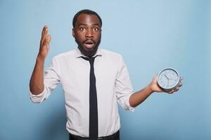 African American male entrepreneur shockingly looking at clock before going for company meeting. Black businessman appears to be in a panic, rushing and experiencing an emergency. photo