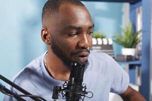 Blogger talking in microphone while recording podcast vlog for internet channel. Young african american man speaking in mic while streaming online in social media networks photo