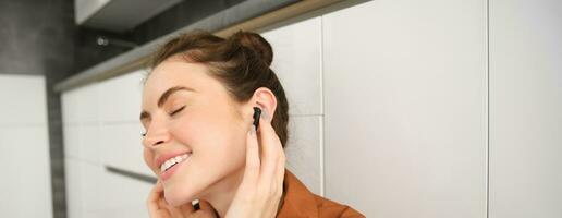 Close up portrait of woman smiling from sound quality in her wireless black earphones, listening to music in headphones, she has pleased face and eyes closed from satisfaction photo