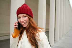 Happy redhead woman, girl with phone talks, has conversation on mobile app, uses internet to call abroad with smartphone app, laughing and smiling photo