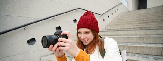 Urban people and lifestyle. Happy redhead woman takes photos, holding professional digital camera, photographing on streets photo