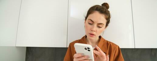 Close up portrait of woman looking at her smartphone with thoughtful face, online shopping, buying something on the internet using mobile app photo