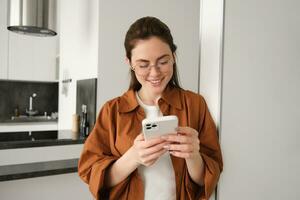 Beautiful woman checking social media while using smartphone at home. Smiling young female using mobile phone app and playing game, shopping online or reading news. Copy space photo