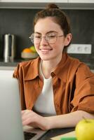 Vertical shot of woman working from home, business owner using laptop, browsing social media on computer, wearing glasses photo