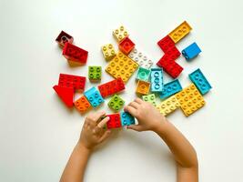 Child playing with colorful building blocks on a white background. Top view photo