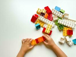 Child playing with colorful building blocks on white background. Top view photo