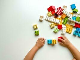 Child playing with colorful building blocks on white background. Top view photo