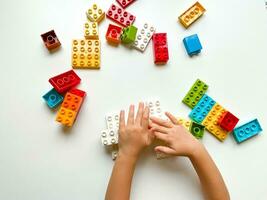 Child playing with colorful building blocks on white background. Top view photo