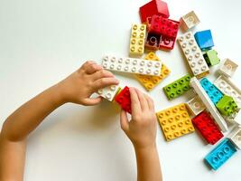 Child playing with colorful building blocks on white background. Top view photo